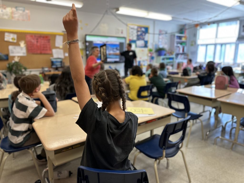 Une élève a la main levée dans une classe